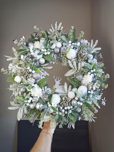 a hand holding a wreath with white flowers and greenery