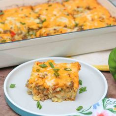 a white plate topped with a casserole covered in cheese and vegetables next to a baking dish