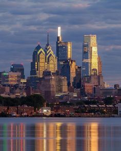 the city skyline is reflected in the water at dusk, as seen from across the bay