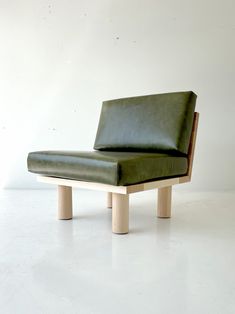 a green leather chair sitting on top of a wooden frame in front of a white wall