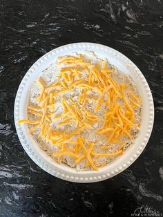 a white bowl filled with cheese on top of a black counter next to a knife and fork