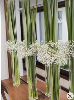 three clear vases filled with baby's breath flowers sitting on a wooden table