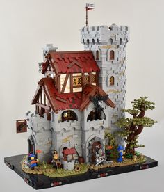 a castle made out of legos on top of a white surface with trees and people