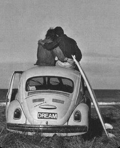 two people sitting on top of an old vw bug in front of the ocean