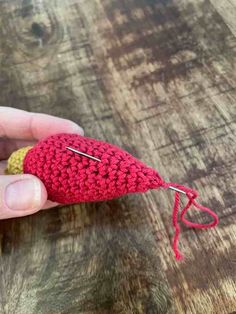 someone is holding a crocheted red object in their left hand and there are two pins sticking out of it