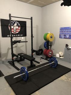 a gym room with two squat racks, barbells and a flag hanging on the wall