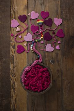 a bowl filled with yarn and hearts on top of a wooden table next to a wall