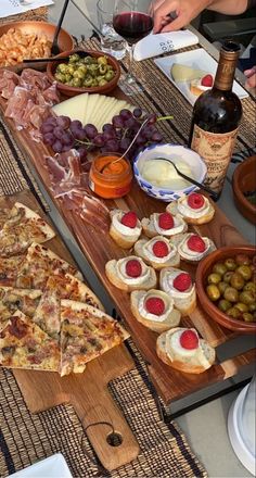 an assortment of food is displayed on a table with wine and cheeses in bowls