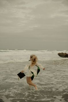 a woman is running in the water at the beach with her hand on her hip