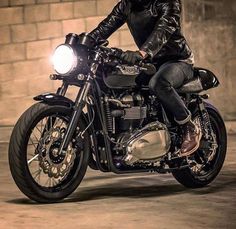 a man riding on the back of a motorcycle down a street next to a brick wall