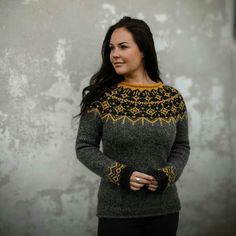 a woman standing in front of a wall wearing a sweater