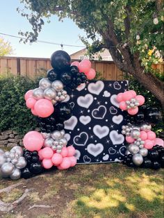 balloon arch with hearts and balloons on it in front of a fenced backyard area