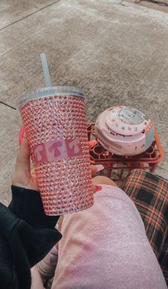 a person holding up a pink cup next to a donut