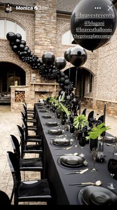 a table set up with black balloons and place settings for an elegant dinner party in front of a brick building