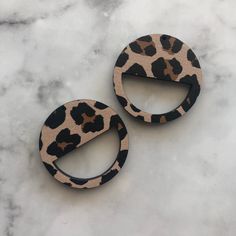 two leopard print wooden earrings sitting on top of a marble surface