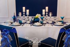 a table set with blue and white plates, silverware and candles for a formal dinner