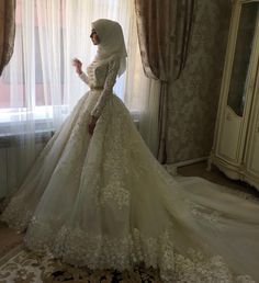 a woman in a wedding dress standing by a window