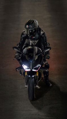 a man riding on the back of a motorcycle down a street at night with its lights on