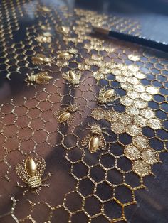 gold beaded mesh with golden bees on it and a pen laying next to it