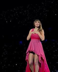 a woman in a pink dress standing on stage with her arms crossed and legs crossed