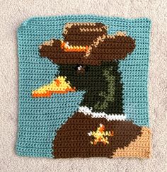 a crocheted square with an image of a duck wearing a cowboy hat and holding a carrot