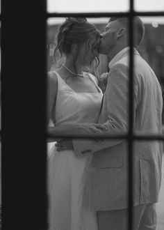 a bride and groom kissing in front of a window