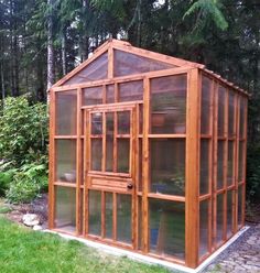 a small wooden greenhouse in the middle of a yard with grass and trees around it