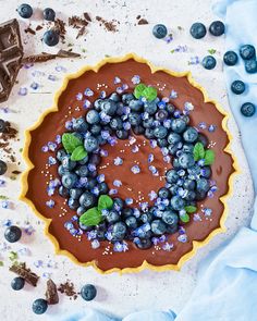 a chocolate tart topped with blueberries and mints on top of a table