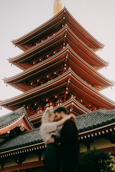 a woman holding a baby in front of a tall building with a pagoda on top