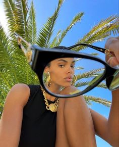 a woman in black dress holding up her glasses with palm trees in the back ground