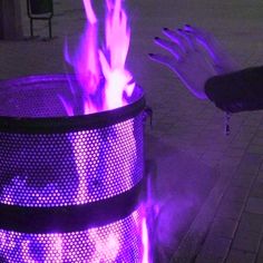 a purple trash can with flames coming out of it and someone's hand on top