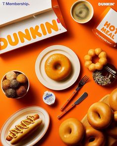 an orange table topped with doughnuts and other foods next to a dunkin donut box