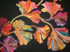 an art quilt with colorful flowers and leaves on black fabric, in the shape of a flower