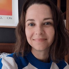 a close up of a person wearing a sweater and posing for a photo in front of a book shelf