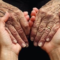 two older hands holding each other with their fingers folded in front of one another and the other