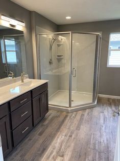 a large bathroom with a walk in shower next to a white sink and wooden floors