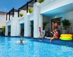 two people are playing in the pool while another person swims by on an inflatable raft