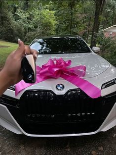 a person holding a cell phone in front of a car with a pink ribbon on it