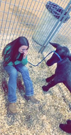 a woman sitting on the ground next to a dog in a fenced in area