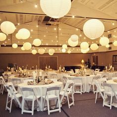 there are many white paper lanterns hanging from the ceiling in this wedding reception room with tables and chairs