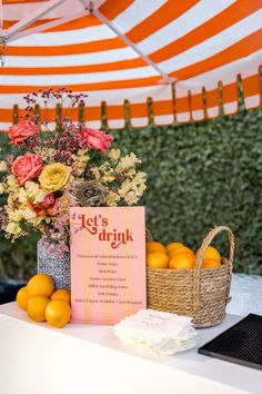 an orange and white striped umbrella next to a table filled with lemons and flowers