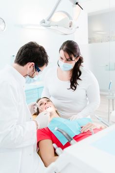 two dentists examining a woman's teeth in the dental room with her patient