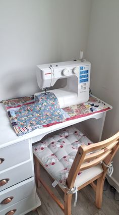 a sewing machine sitting on top of a white table next to a chair and drawer