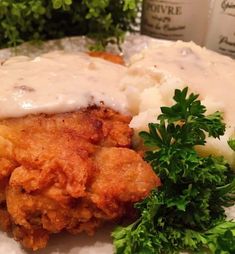 fried chicken with gravy and mashed potatoes on a plate next to parsley