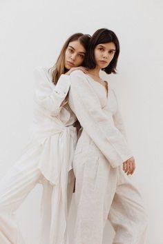 two women standing next to each other wearing white clothing and one has her arms around the other