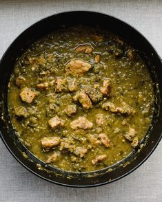 a black pan filled with meat and green sauce on top of a white table cloth