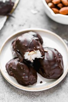 three chocolate covered donuts on a plate with almonds in the bowl behind them