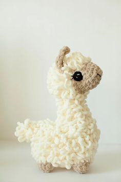 a crocheted llama stuffed animal sits on a white surface with black eyes