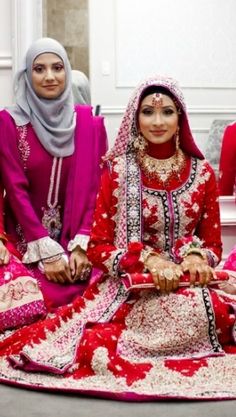 three women dressed in red and pink sitting on the floor with one woman wearing a headscarf