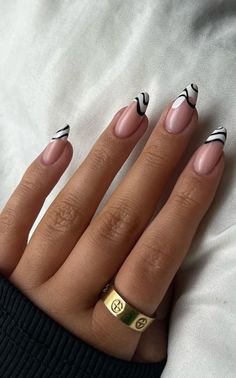 a woman's hand with black and white nail polish on it, holding a gold ring